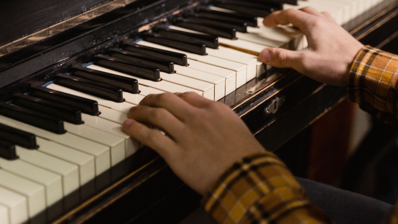 Hands in a plaid flannel shirt practicing on a worn vintage upright piano at home