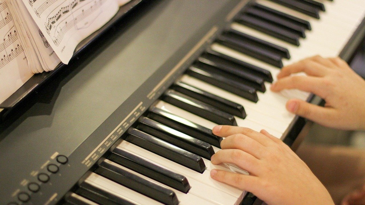 Young piano student's hands practicing a scale on a digital piano, with an open music book on the stand