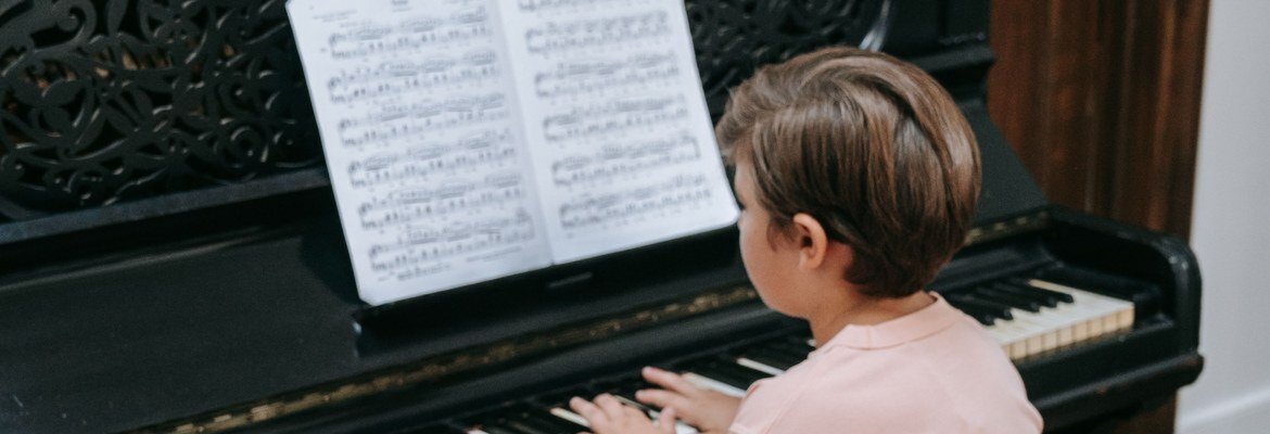 Young boy practicing from sheet music at an old black upright piano at home