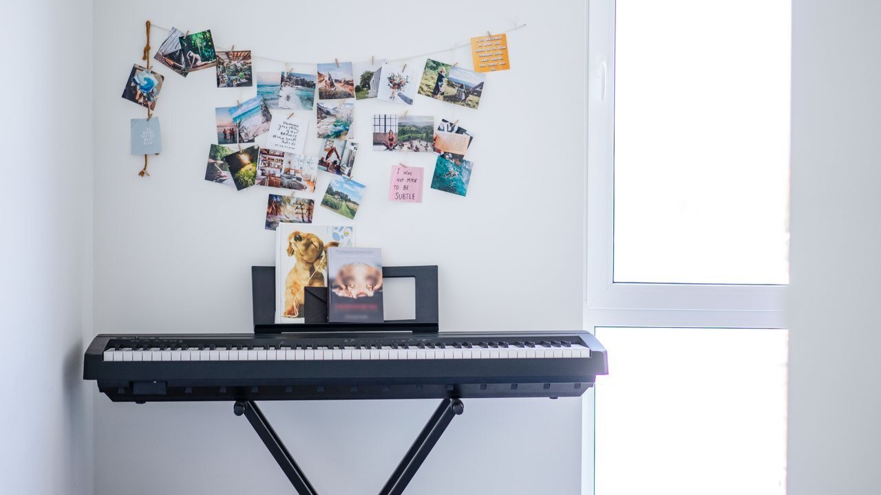 Portable slab digital piano on an X-stand with a music rest in a bright room with photos on the wall