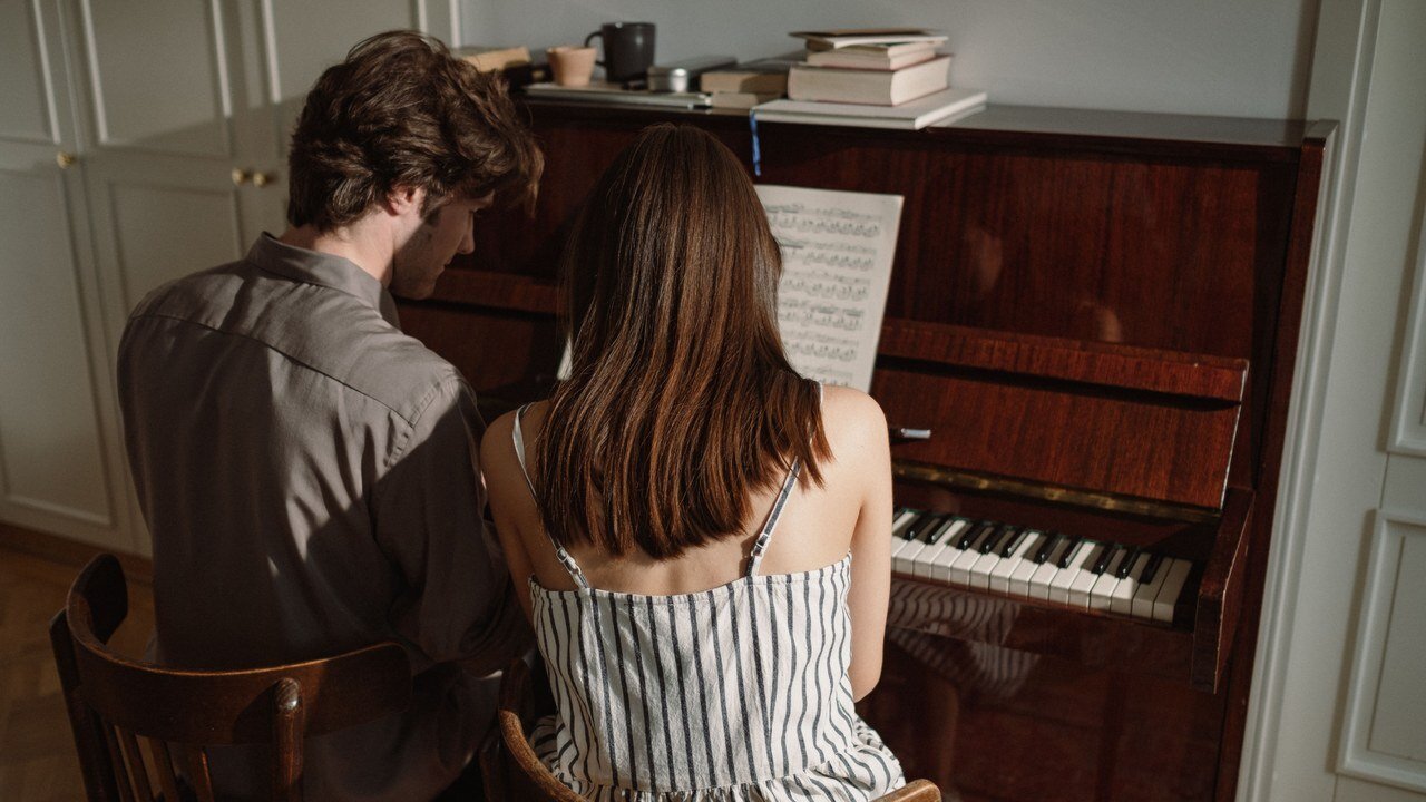 Teacher and student sitting side by side at an upright piano during a lesson