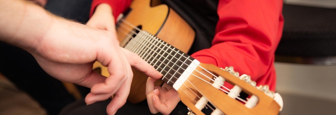 Teacher's hand guiding a child's fingers on a classical guitar during a one-on-one music lesson