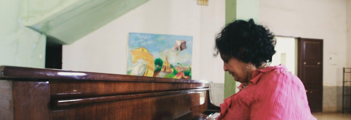 Mature woman smiling as she plays an old wooden piano in a bright community hall