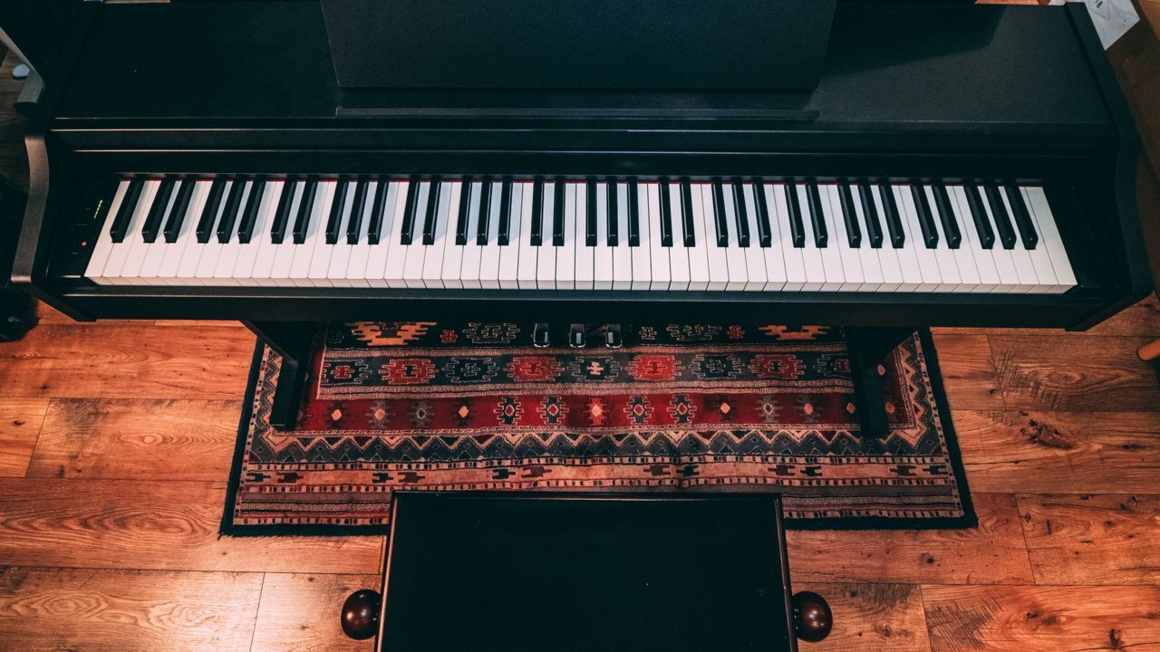 Black console digital piano with three pedals and a matching bench on a patterned rug