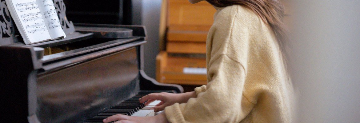 Beginner practicing at an open upright piano with sheet music