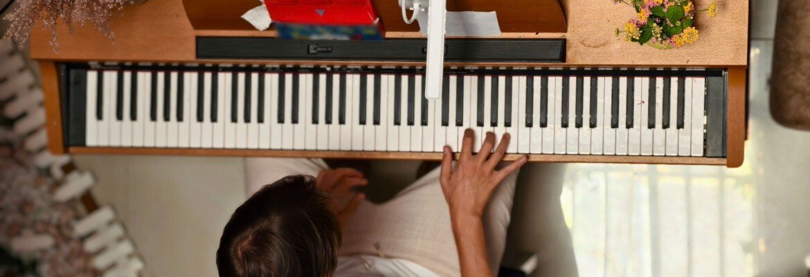 Adult practicing alone at a wooden digital piano at home, seen from above, flowers on the lid
