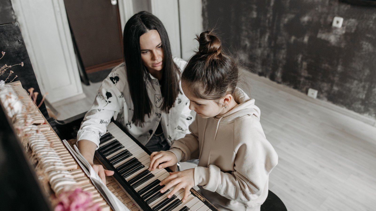 Piano teacher sitting beside her student at the keys, watching her hands during an exam-prep lesson