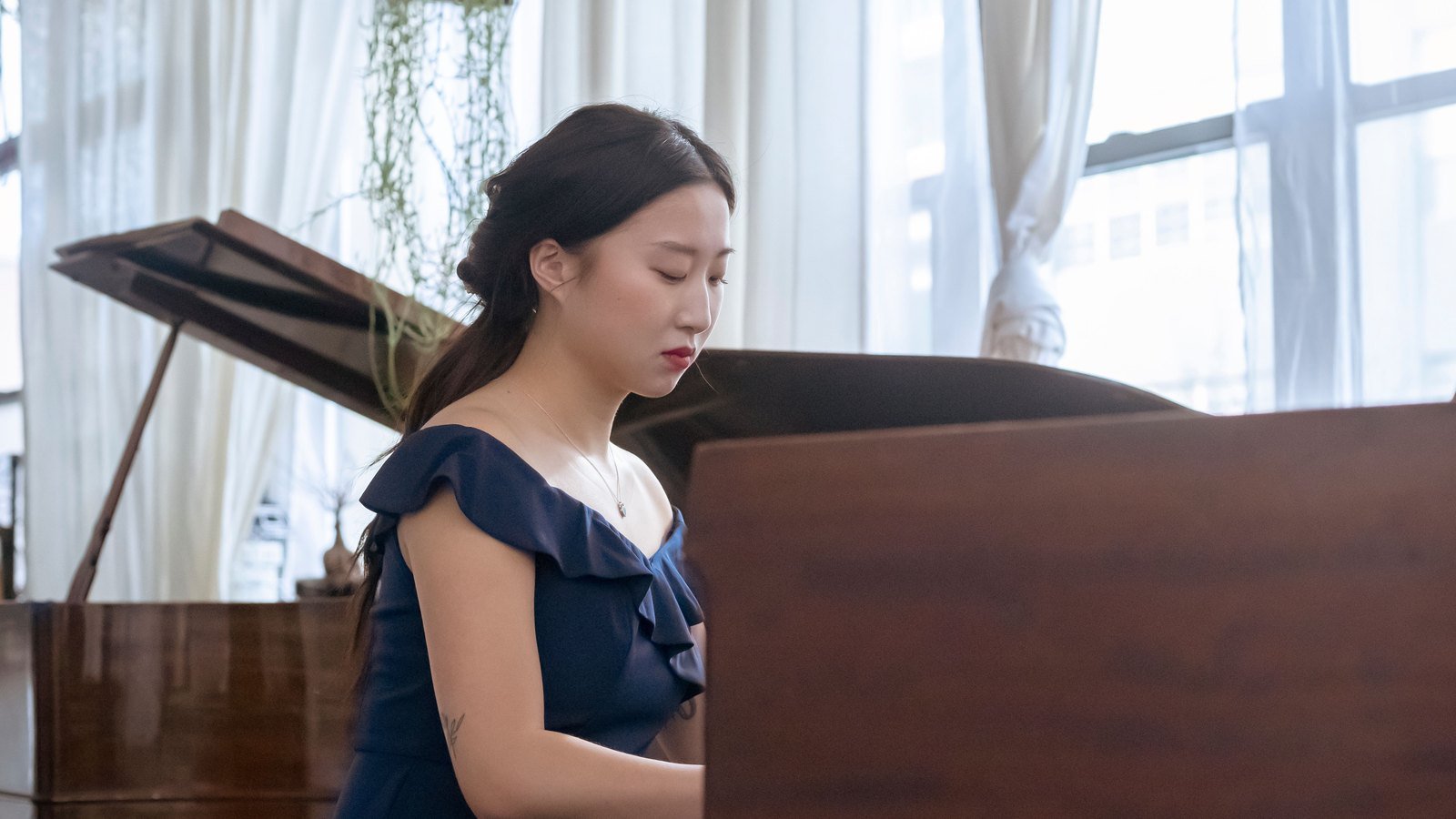Piano student in a recital dress practicing her audition repertoire at a grand piano