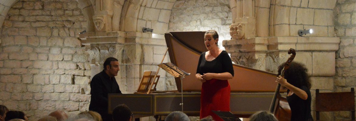 Audience watching a singer, keyboardist and double bass player perform in a vaulted stone hall