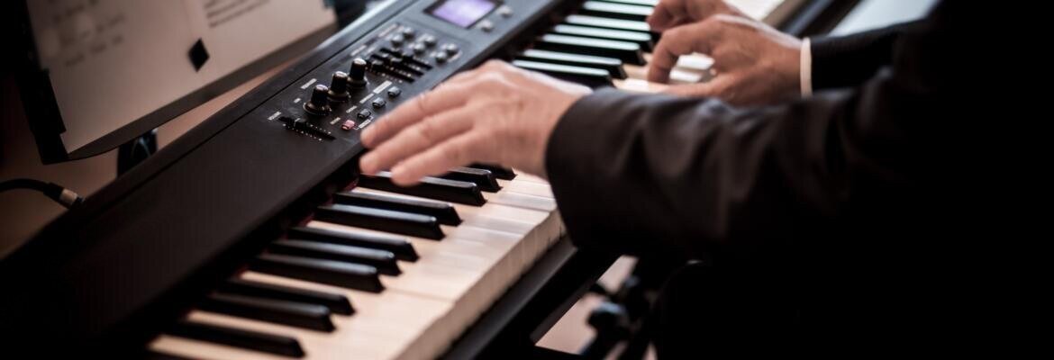 Hands playing a black stage digital piano with handwritten sheet music on the stand