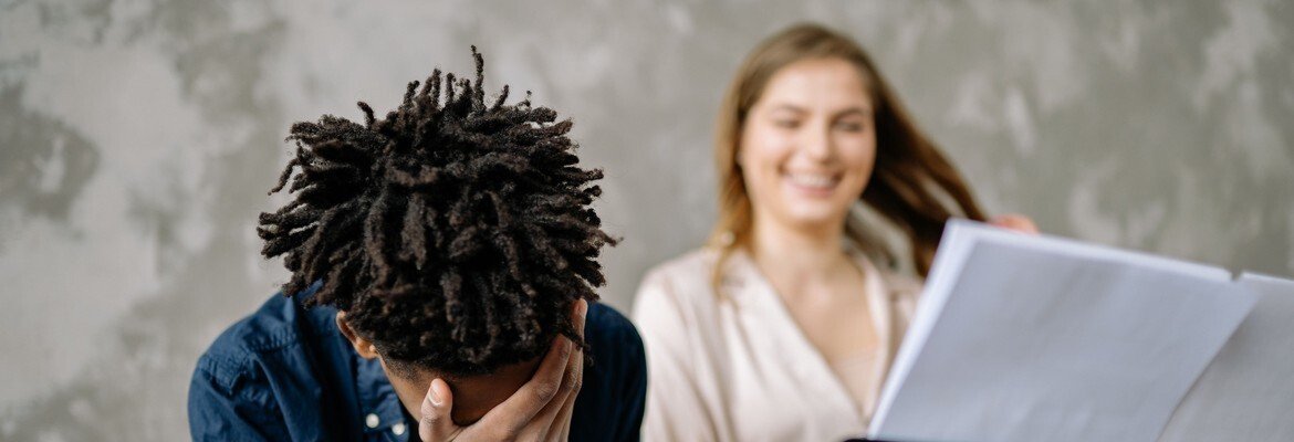 Frustrated piano student hides his face in his hand while his teacher holds up sheet music behind