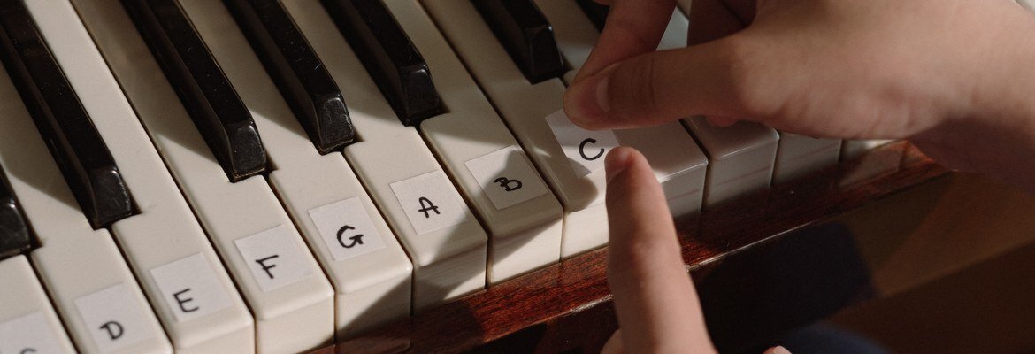 Hands pressing a paper C sticker onto a piano key next to keys labeled D through B