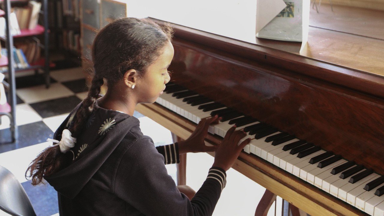 Intermediate-age piano student practicing with both hands on an older wooden piano